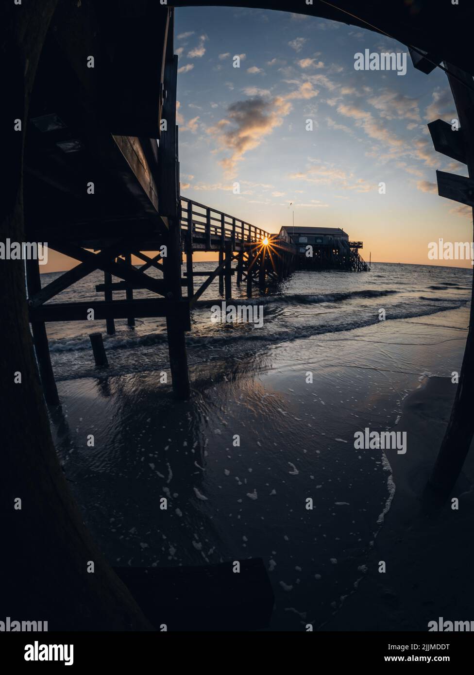 A vertical shot of a wooden pier above the ocean on a sunset sky ...