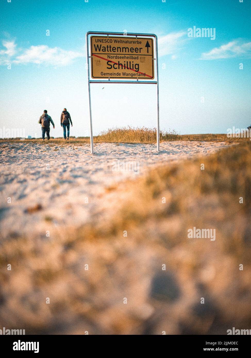 A vertical shot of people hiking and a sign with 'Wattenmeer' writing on blue sky background Stock Photo