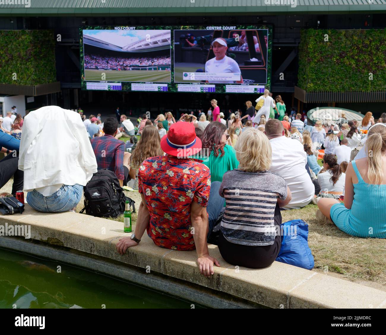 Wimbledon Tennis Championship. Crowds sit on the lawn on The Hill outside number one court watching the action on a big screen. London. Stock Photo