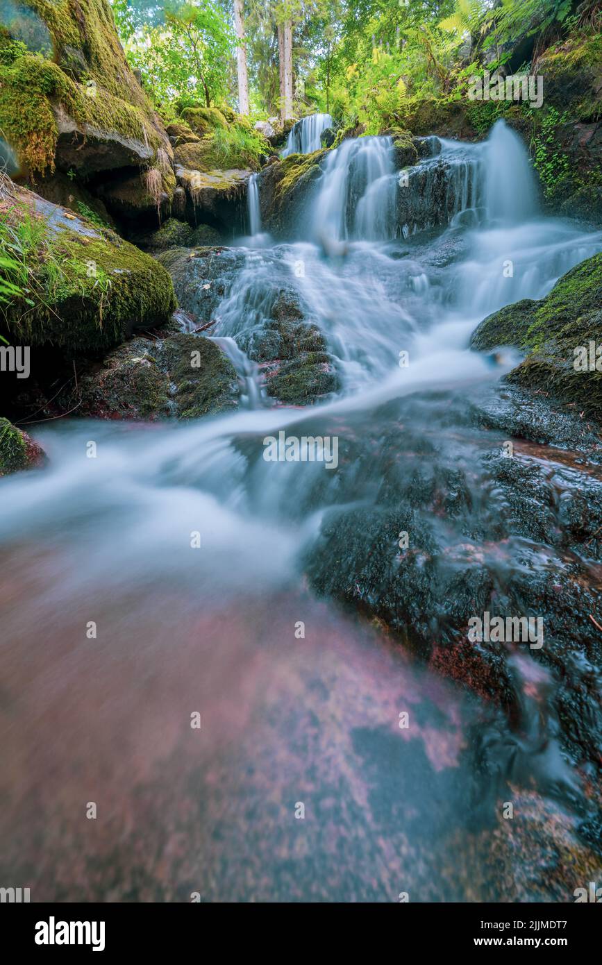 A vertical long exposure shot of a beautiful waterfall flowing on mossy ...