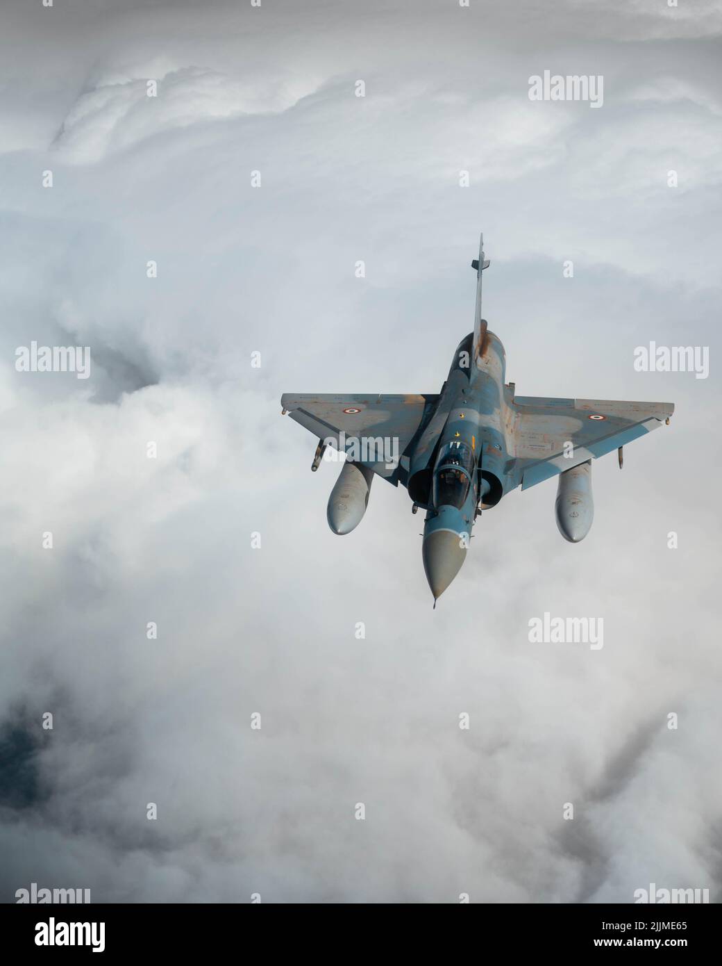 A vertical shot of a Mirage fighting jet flying over the clouds in Las