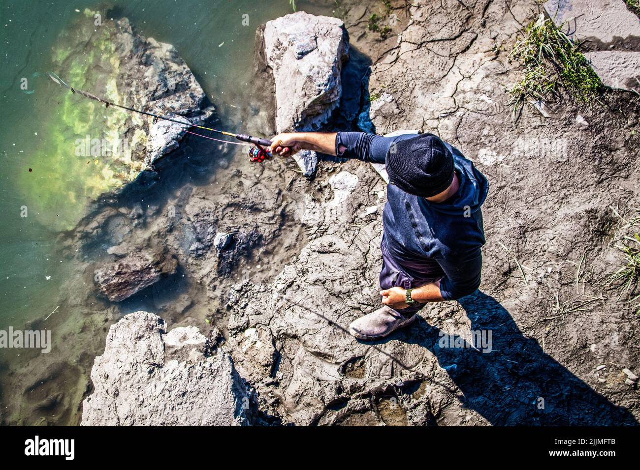 2022 06-25 Anchorage Alaska USA - Top down view of unrecognizable man with cap fishing for salmon in Ship Creek near downtown. Stock Photo