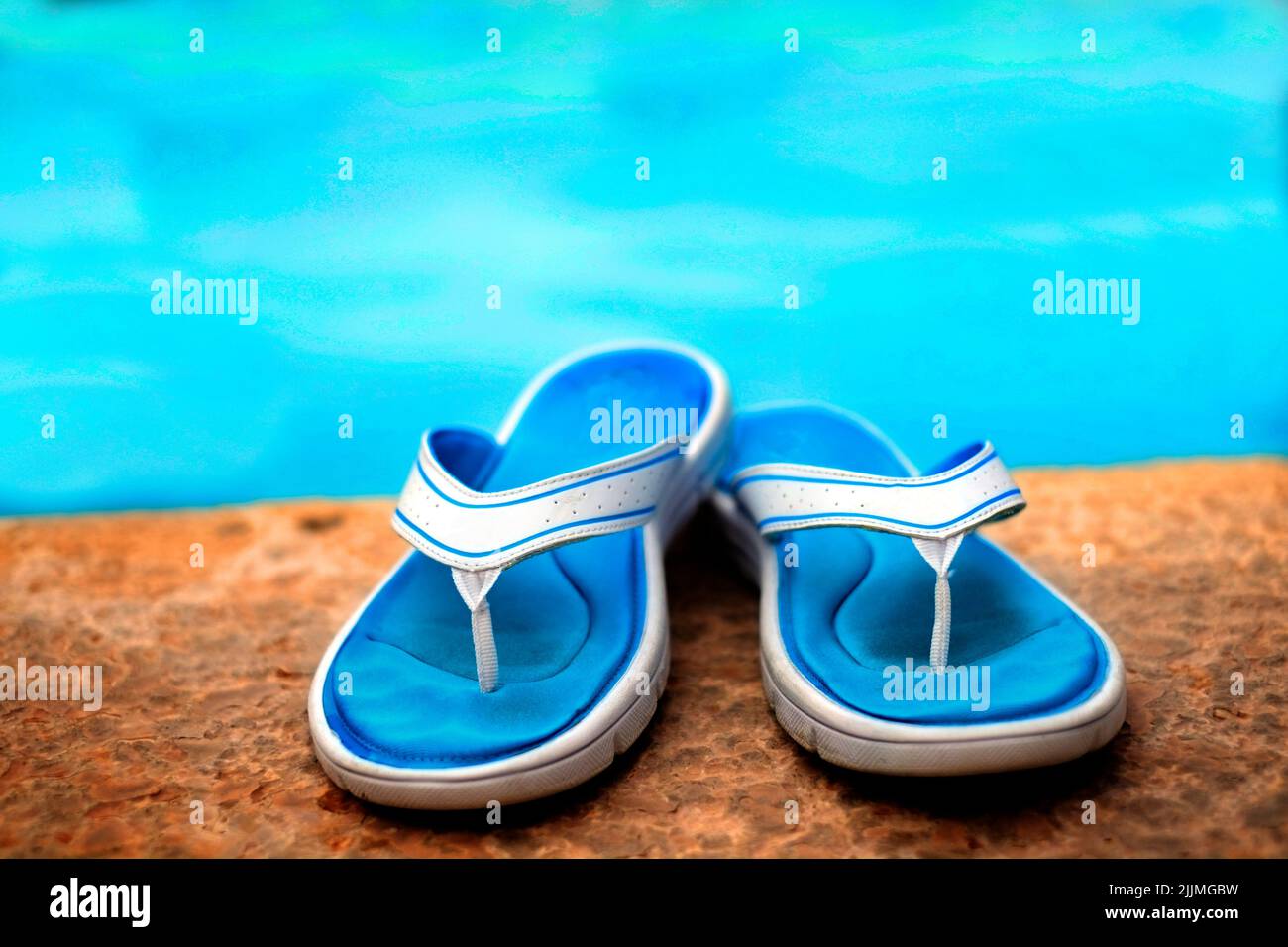 Pair of sandals flip flops next to clear swimming pool with blue water Stock Photo