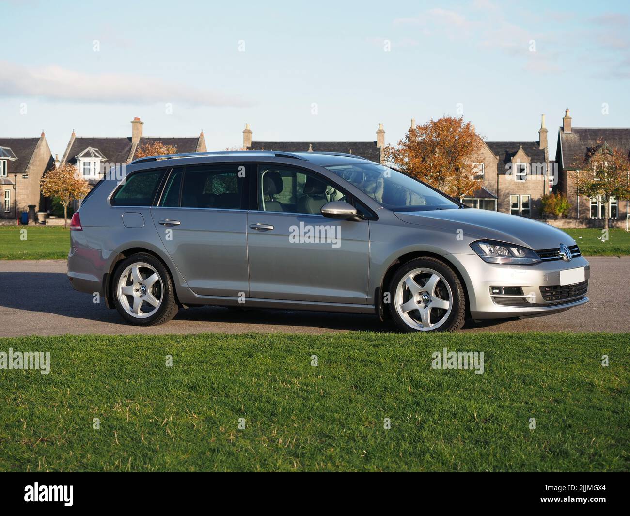 Tungsten silver Volkswagen Golf MK7 estate, variant, with Team Dynamics Pro Race 3 Alloys. Parked next to green grass playing fields. Stock Photo