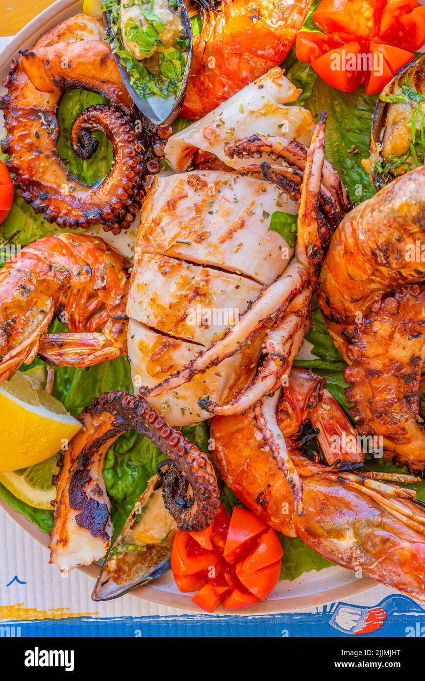 Seafood platter with grilled squid, octopus, prawns and mussels on green salad with lemon and tomato, vertical Stock Photo