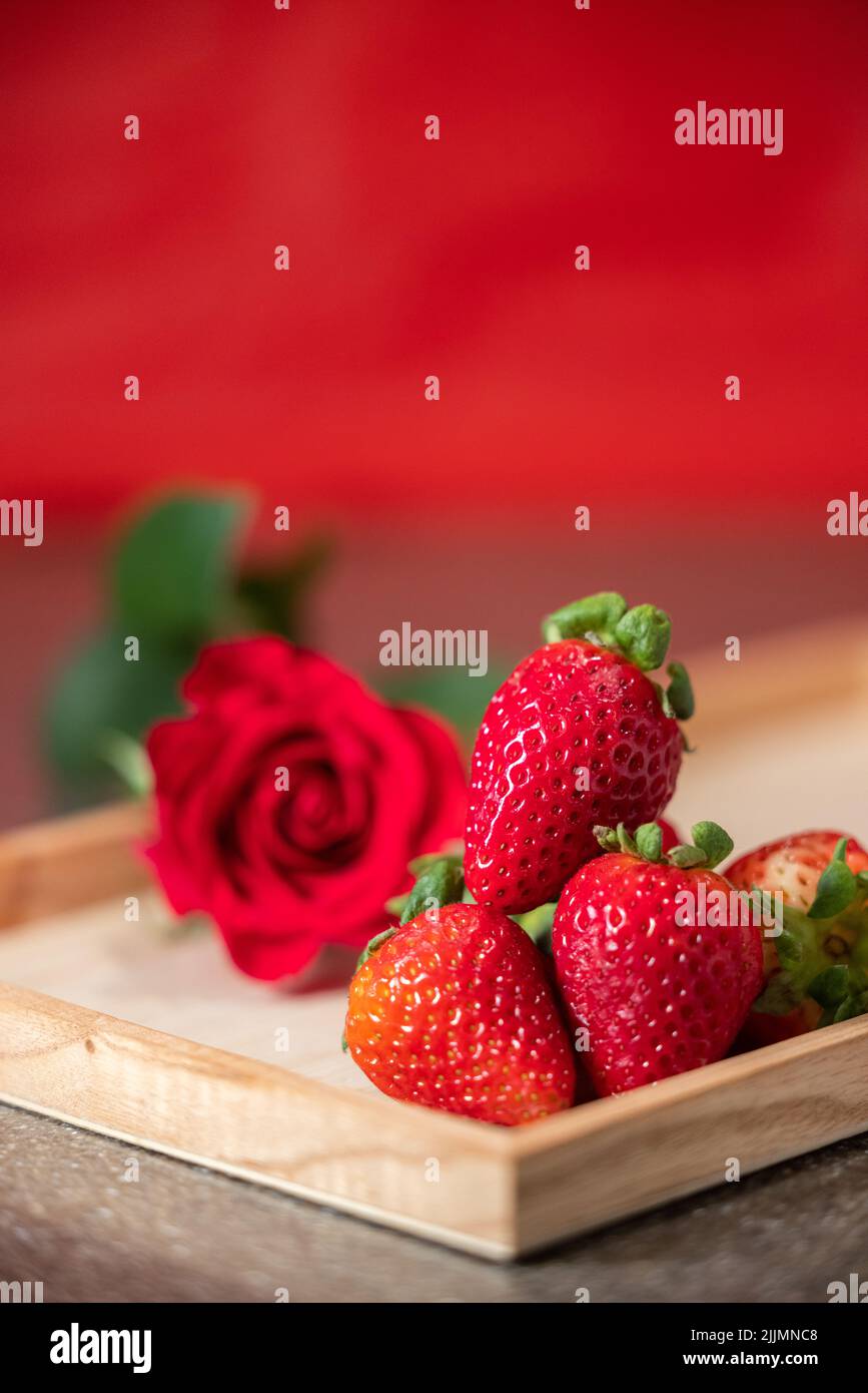 close up of bright red strawberries and a rose in the background as a romantic concept Stock Photo