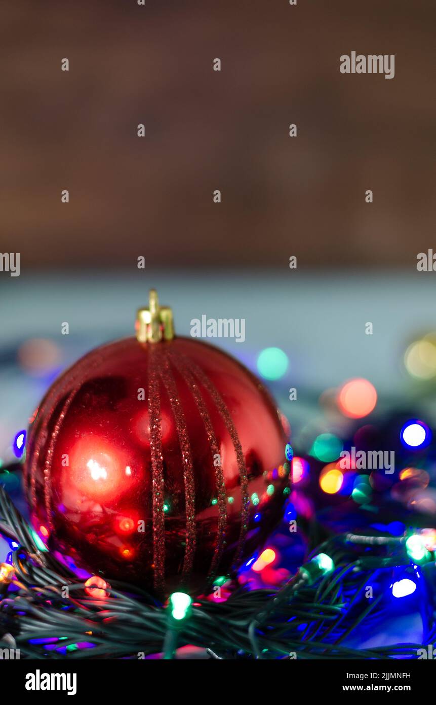 A close-up shot of a red Christmas ball on a string of colorful lights  with a blurred background Stock Photo
