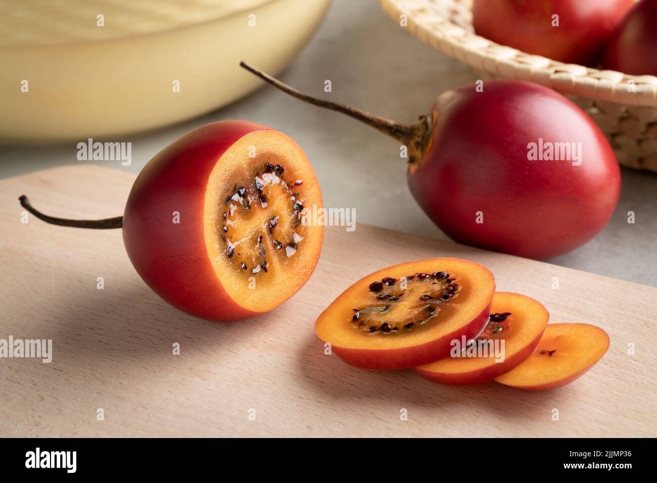 Fresh ripe sliced tamarillo close up on a cutting board and whole ones in the background Stock Photo
