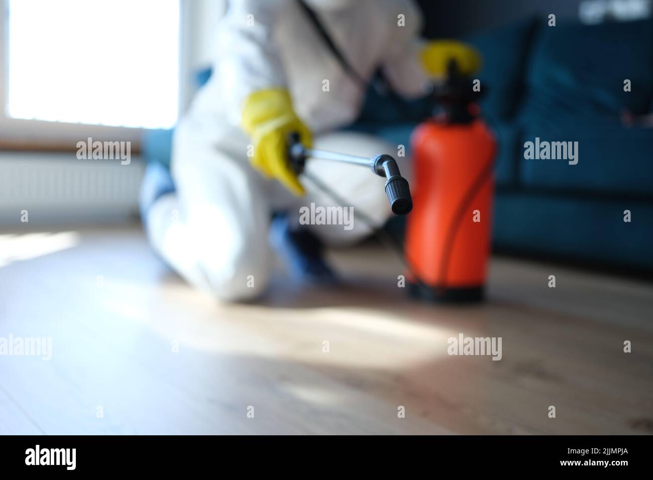 Person in white protective suit in hotel or apartment sprays disinfectant against viruses or rodents Stock Photo