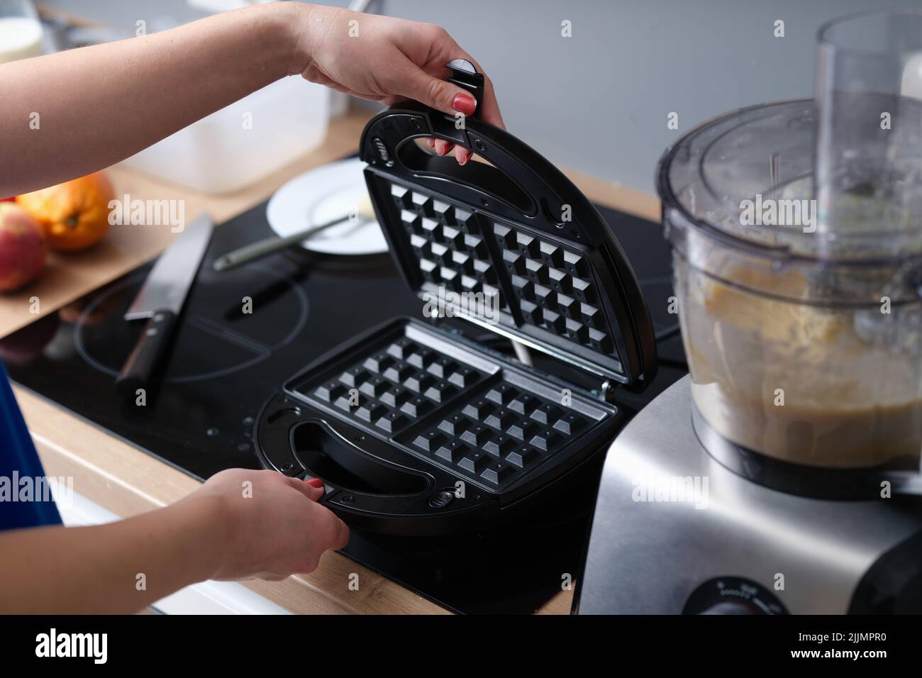Woman has prepared Belgian waffle dough and opens electric waffle iron Stock Photo