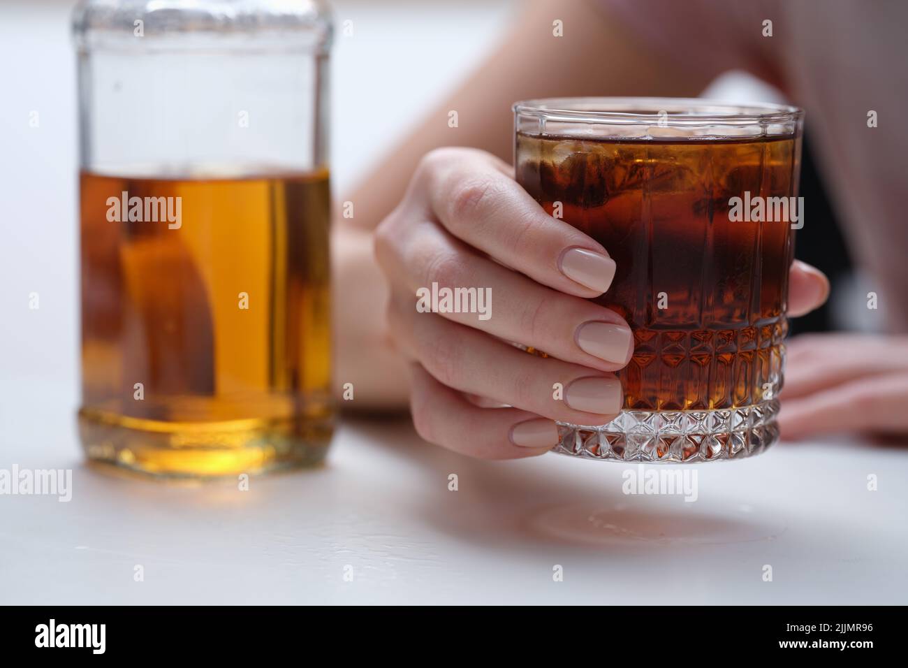 Woman hand holds glass of whiskey or cognac with bottle Stock Photo
