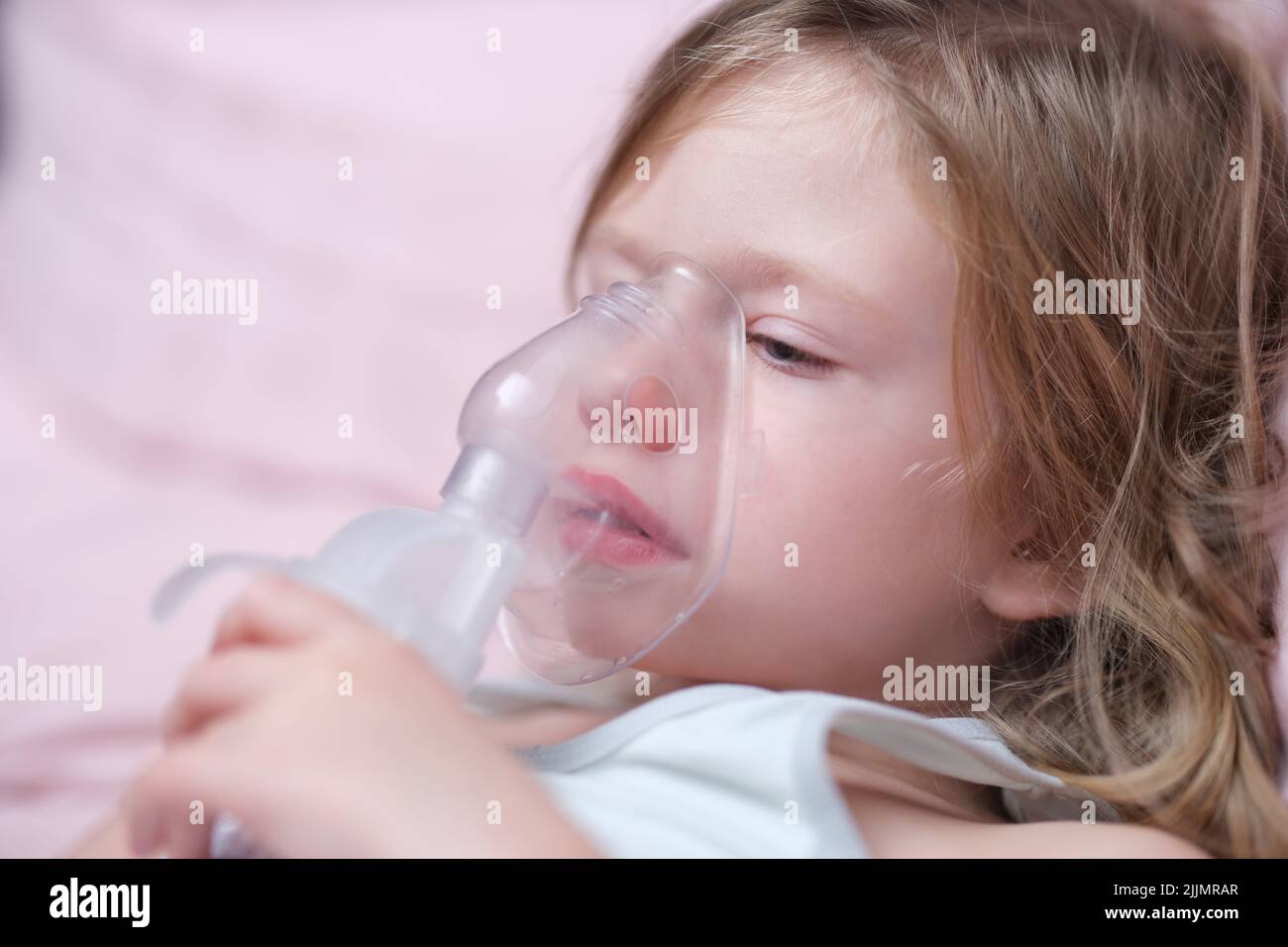 Little baby girl with oxygen mask lying on hospital bed or at home Stock Photo