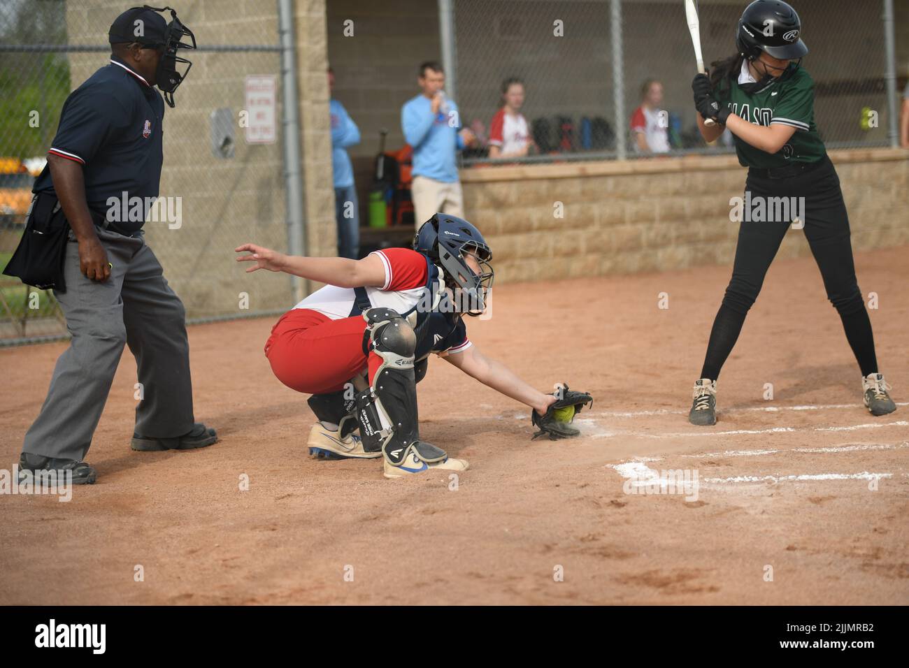 A view of a female catcher playing softball in a red and white uniform