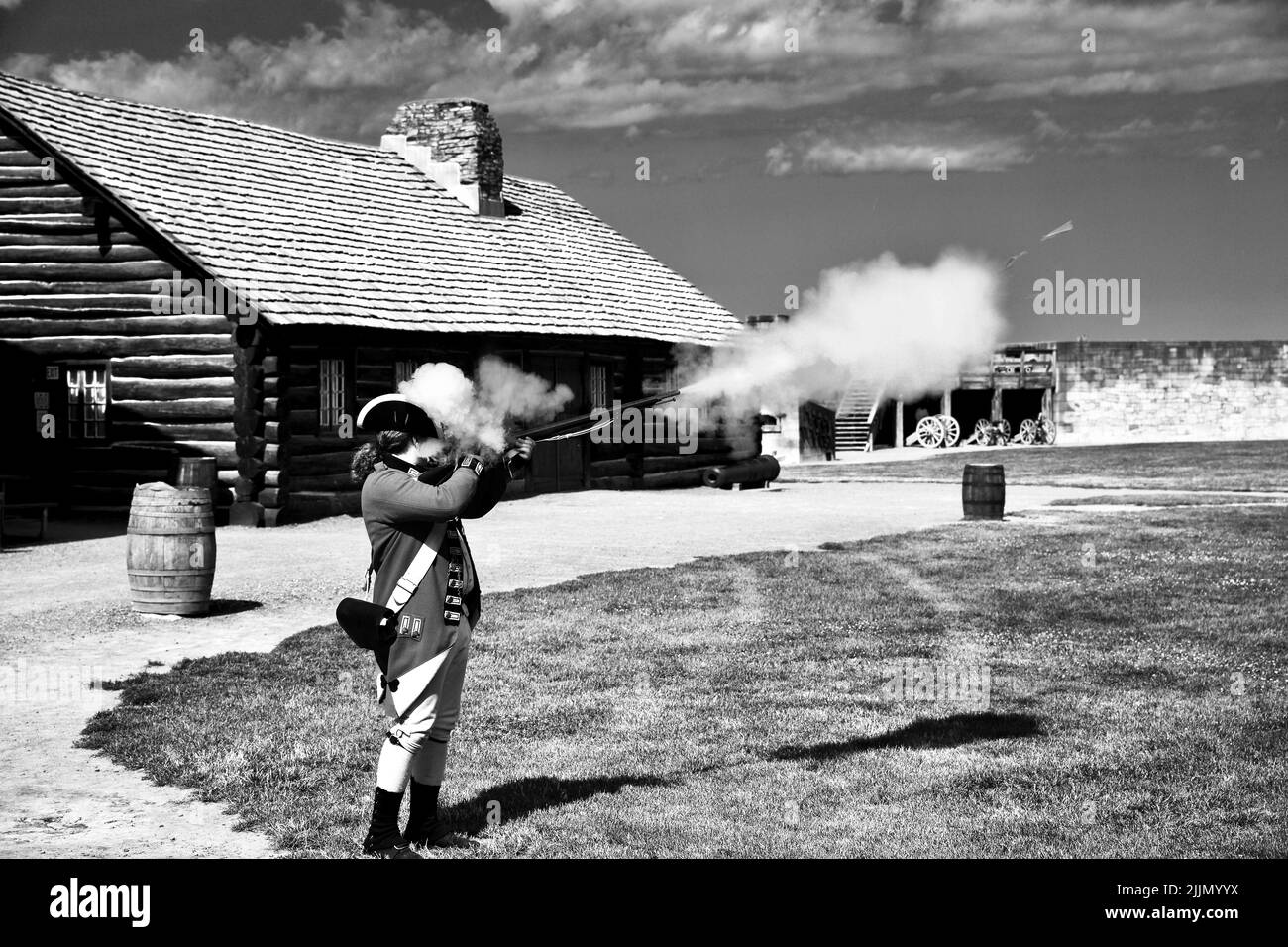A grayscale shot of a man wearing clothes of a french soldier and shooting from the gun. Fort Niagara. Stock Photo
