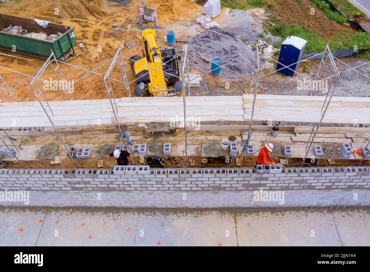 As construction workers work on scaffolding, they lay down masonry