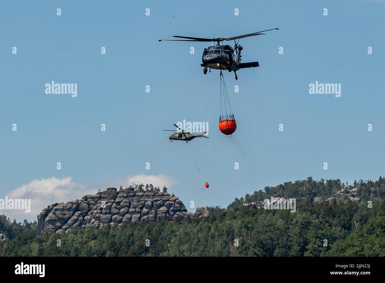 Hrensko, Czech Republic. 27th July, 2022. Helicopters with bambi buckets extinguish large forest fire in the Ceske Svycarsko (Czech Switzerland) National Park, Hrensko, Czech Republic, on July 27, 2022. The fire in the national park has been spreading for the fourth day in a row. Credit: Ondrej Hajek/CTK Photo/Alamy Live News Stock Photo