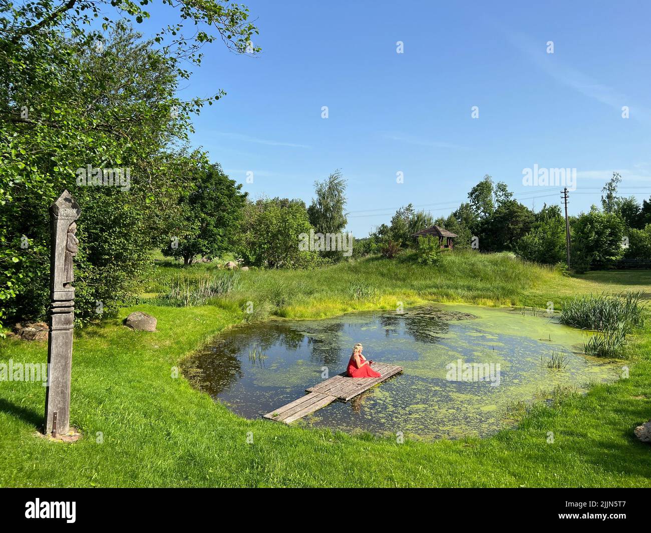 Woman in red dress drinking coffee on a jetty in a lake, Lithuania Stock Photo