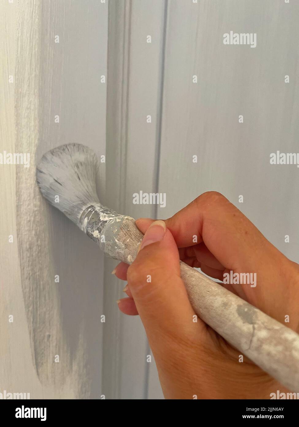 Close-up of a woman painting a doorframe with grey paint Stock Photo