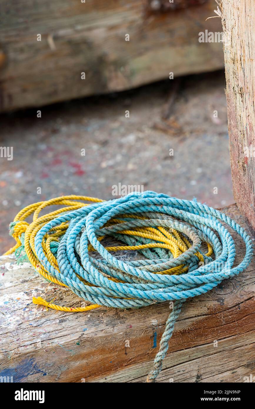 coils of man made nylon rope in yellow and blue plastic material on a quayside in greece, coiled colourful ropes, man made ropes and cordage on wall. Stock Photo