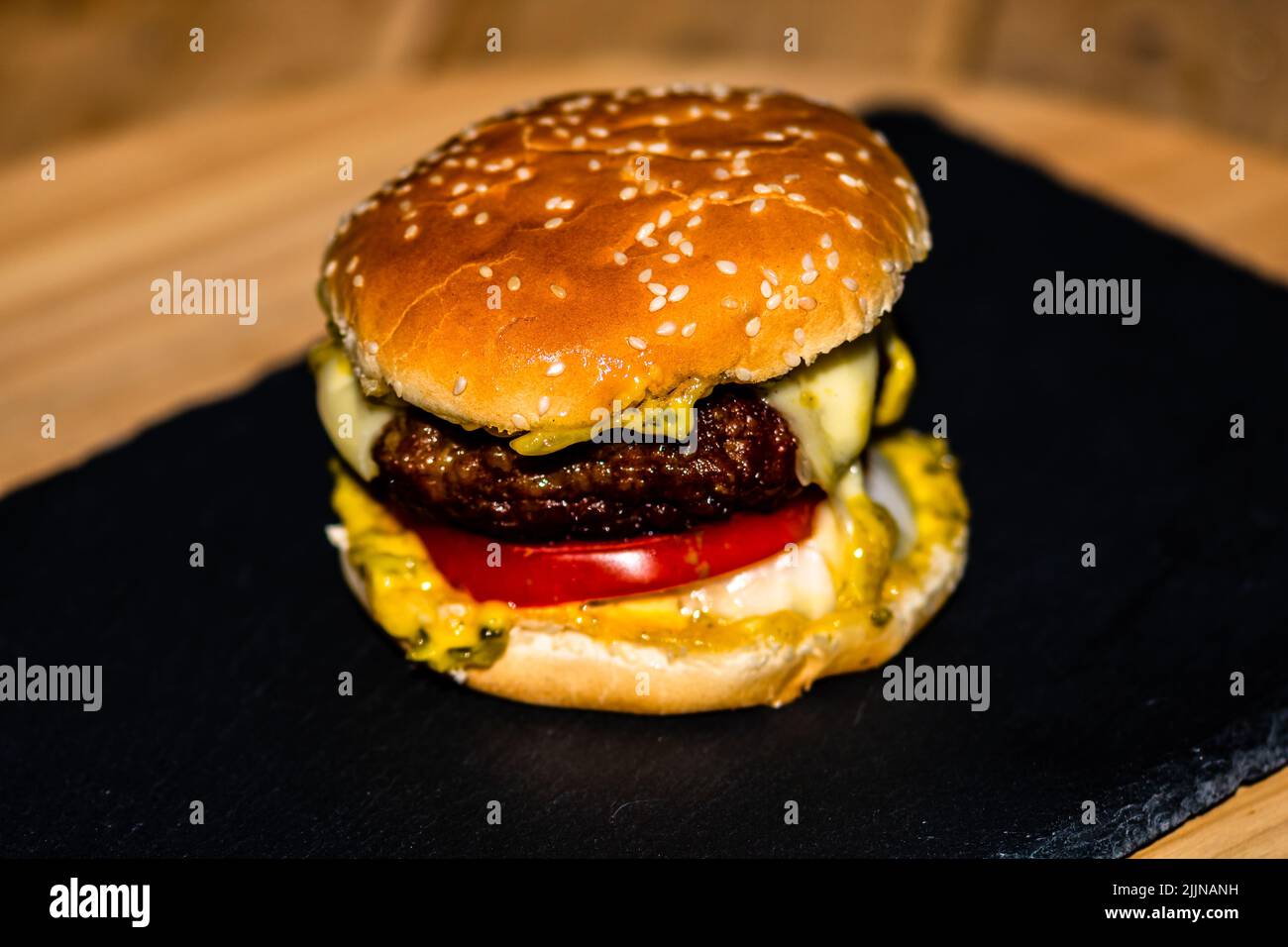 Detail of fresh tasty beef cheeseburger with melted cheese isolated on black background Stock Photo