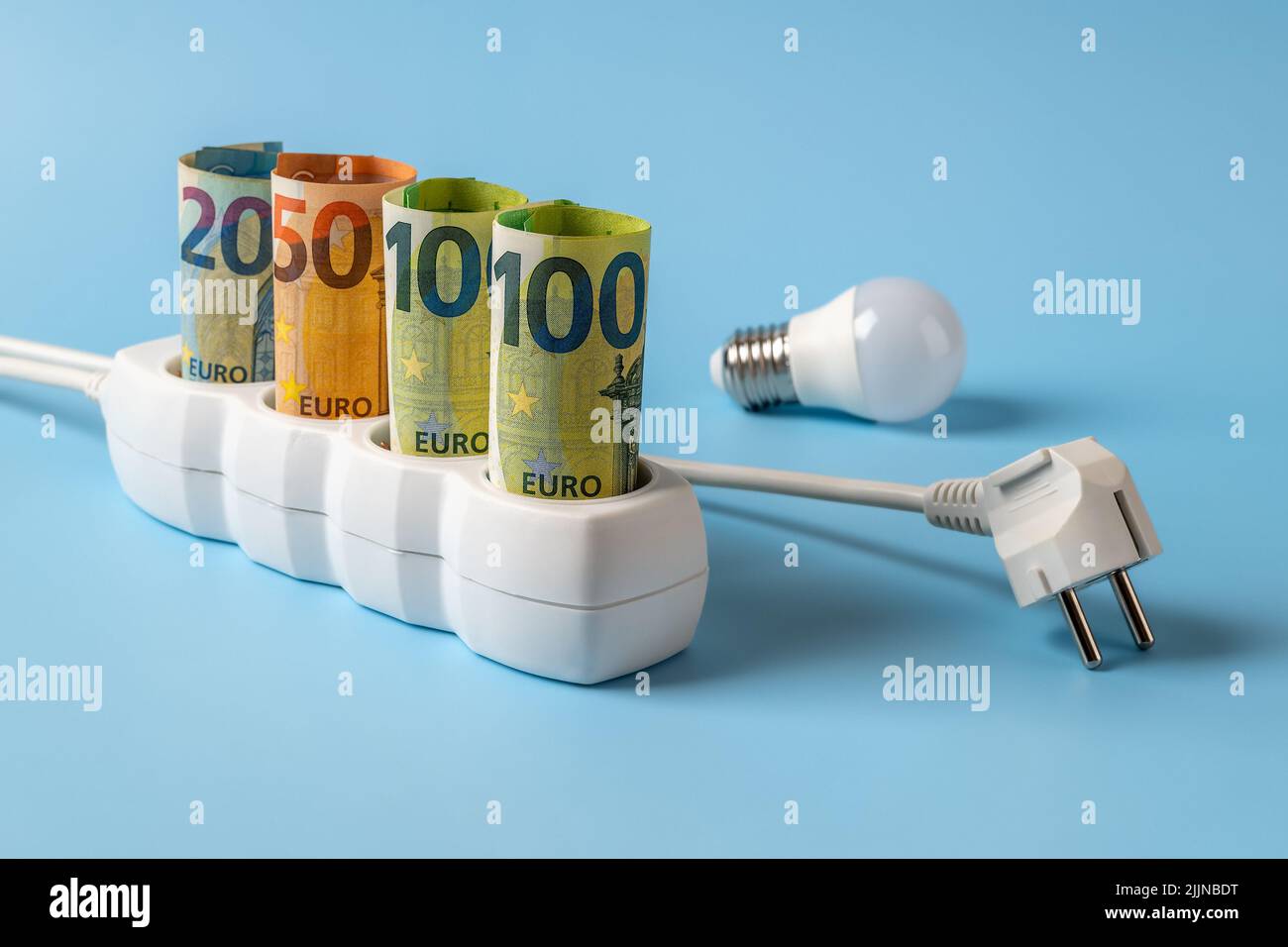 Energy price spike. Rising of electricity bill payment. Euro banknotes plugged into electrical outlet, light bulb and power plug over blue background. Stock Photo