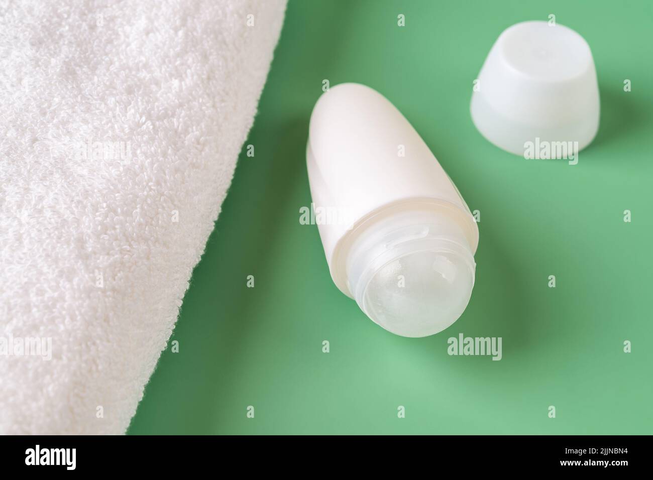 Open roll on antiperspirant deodorant and white bath towel over green background. Body care, toiletries, purity and personal hygiene items concepts. Stock Photo