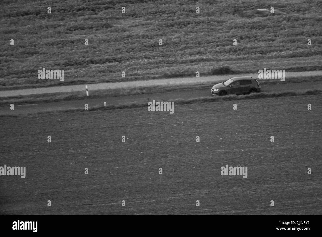 A grayscale of a car riding between fields Stock Photo