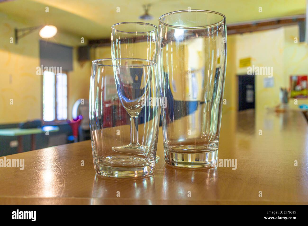 three empty glasses in different sizes and shapes on the counter of a venue with focus on the glasses Stock Photo