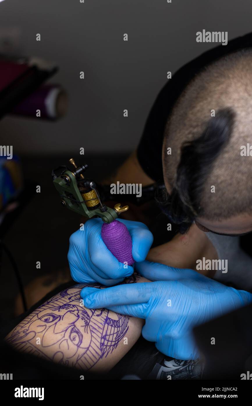 A close-up view of a man tattooing a woman's leg on a stretcher in a tattoo studio Stock Photo