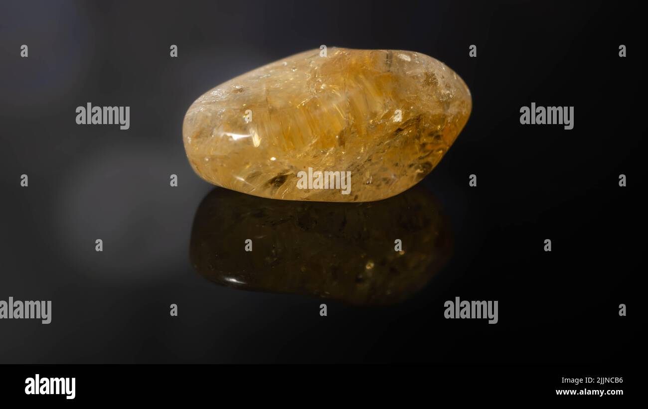 A closeup of a natural gemstone - pebble of citrine mineral gemstone on a reflective surface Stock Photo