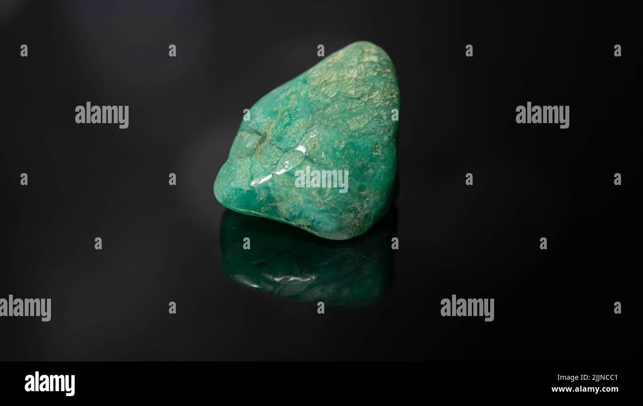 A closeup of a piece of amazonite gemstone on a reflective black ...