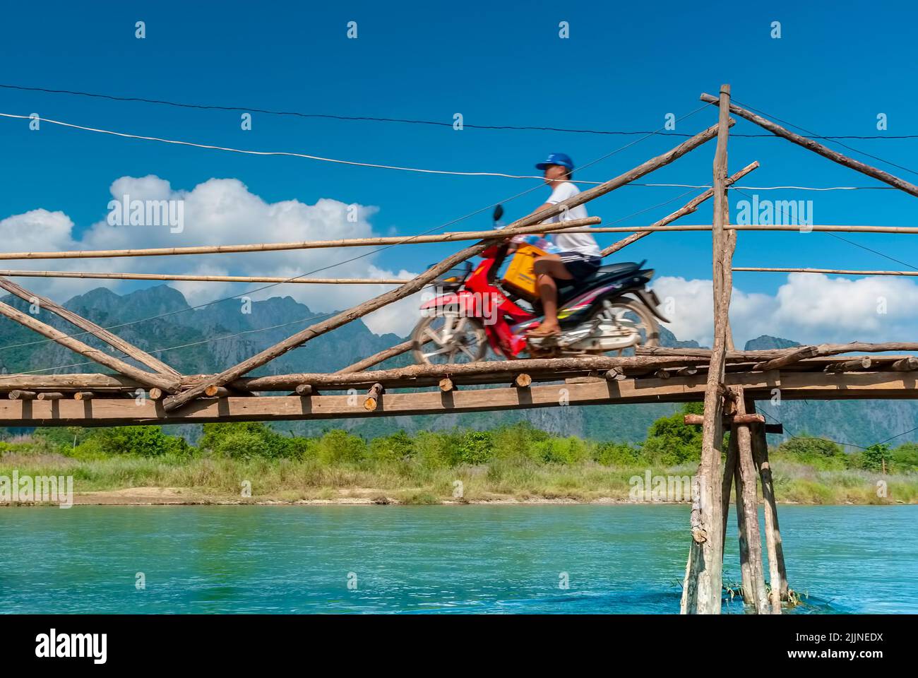 Laotian man transporting beer crate with motorbike over a bridge at the Nam Song River near Vang Vieng Stock Photo