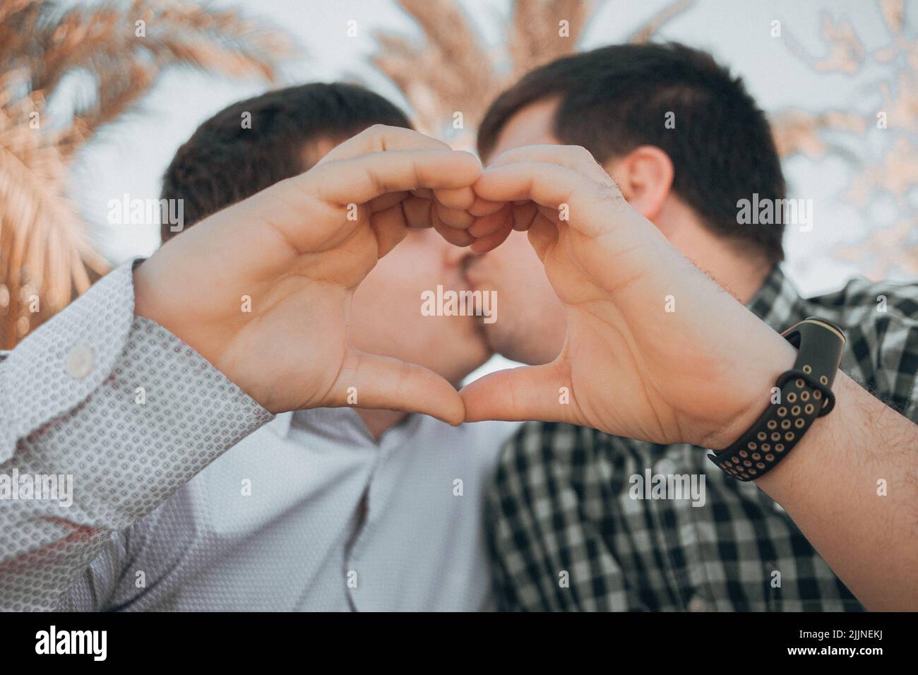 A couple of Spanish men kissing each other while showing hands heart sign - LGBT concept Stock Photo