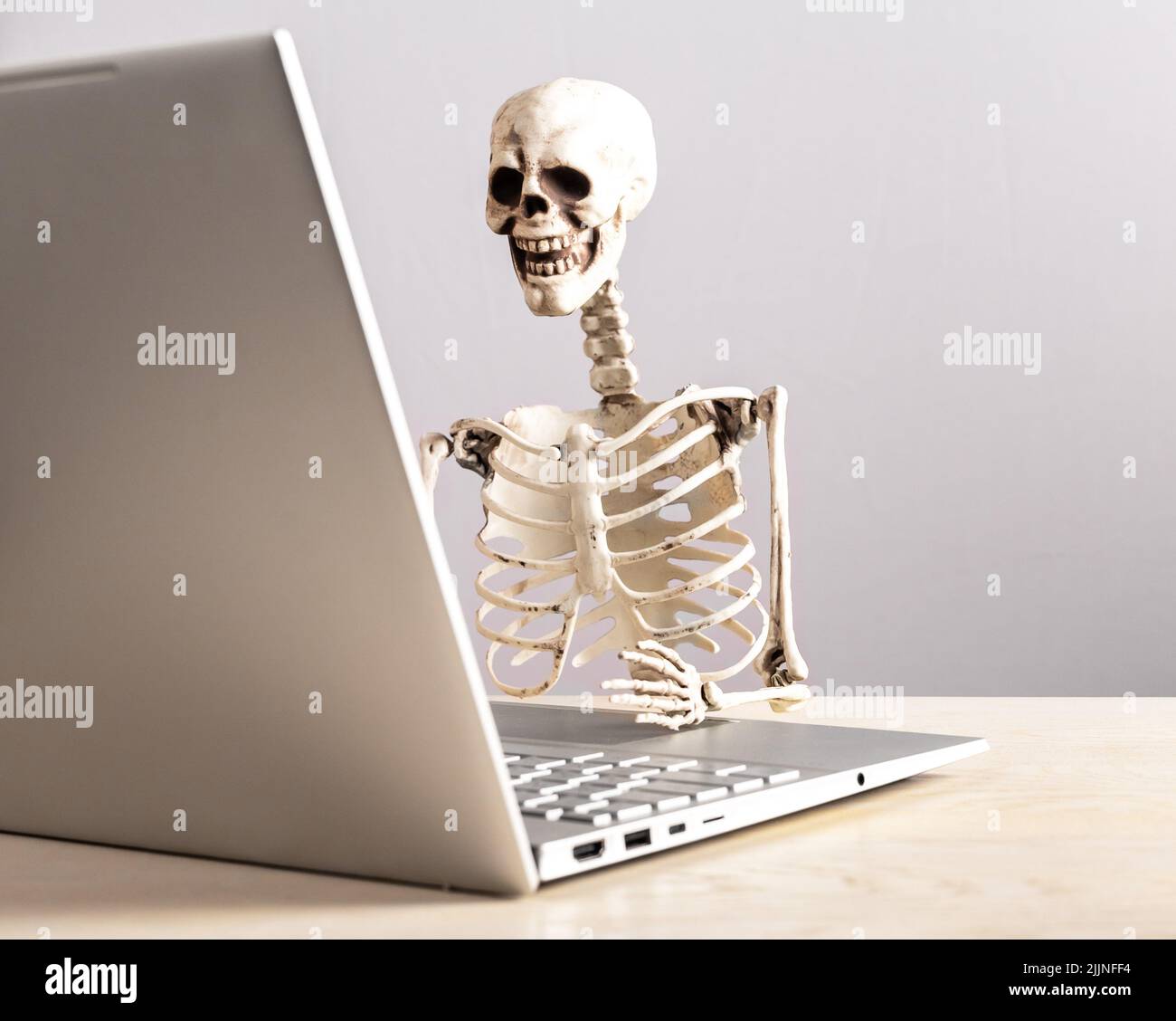 Job burnout. Skeleton sitting at table with laptop. Computer geek. Person suffering from stress at work. Mental and physical exhaustion, fatigue. High quality photo Stock Photo