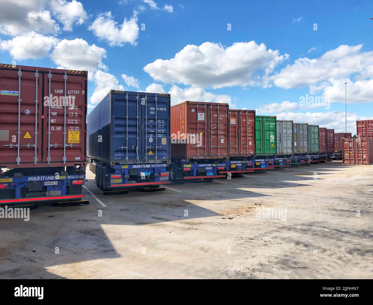 A row of shipping containers loaded onto road transport trucks for onward movement to terminals and docks Stock Photo