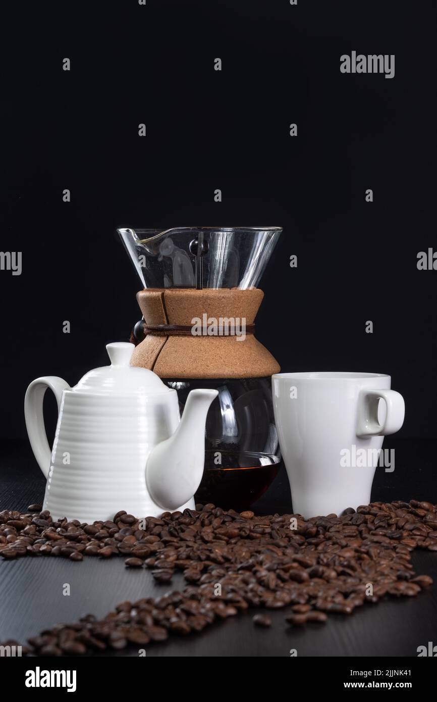 A vertical shot of the chemex coffeemaker with white cup and pot and coffee beans on the table Stock Photo
