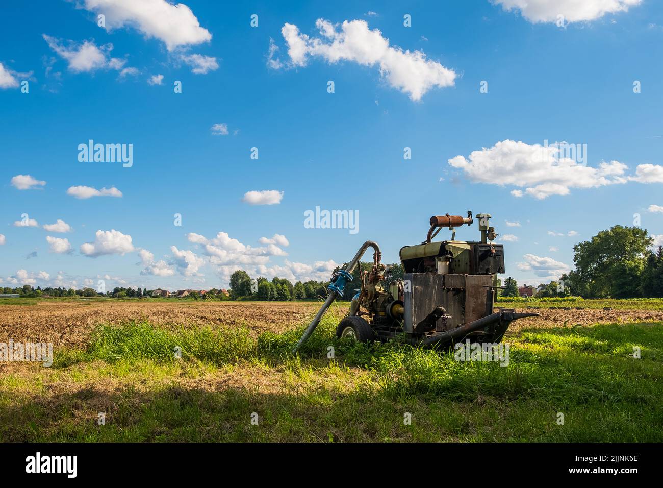 The old farming equipment on the green field against the blue sky Stock