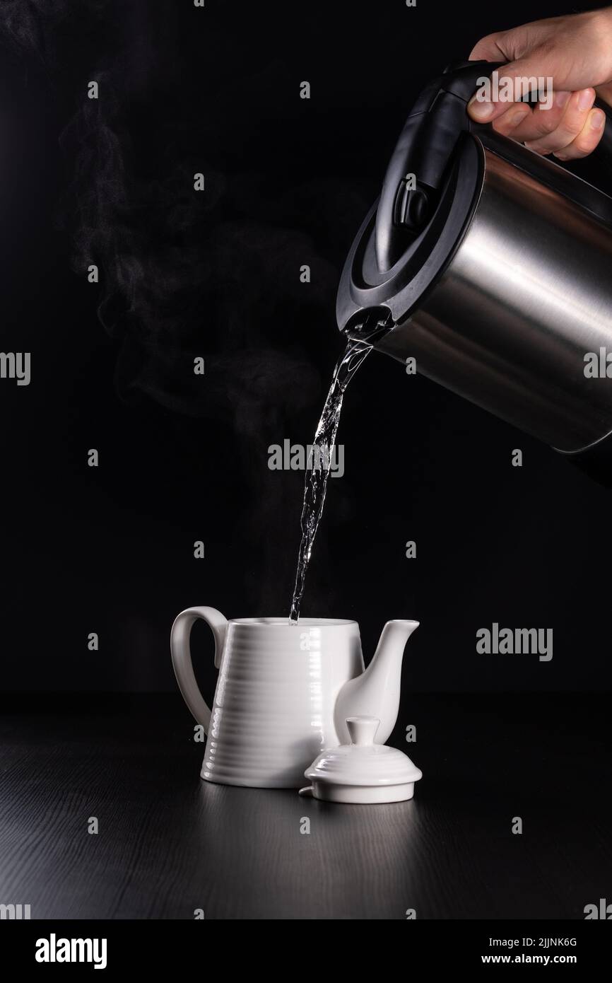 https://c8.alamy.com/comp/2JJNK6G/a-vertical-closeup-of-the-hand-pouring-the-boiling-water-into-a-jug-on-black-background-2JJNK6G.jpg
