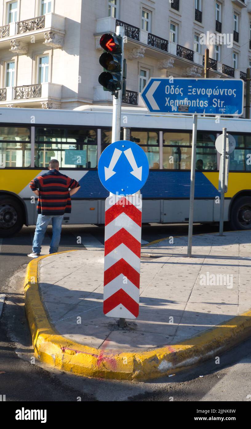 A vertical shot of a bypass road sign, traffic lights and a man waiting in front of a bus Stock Photo