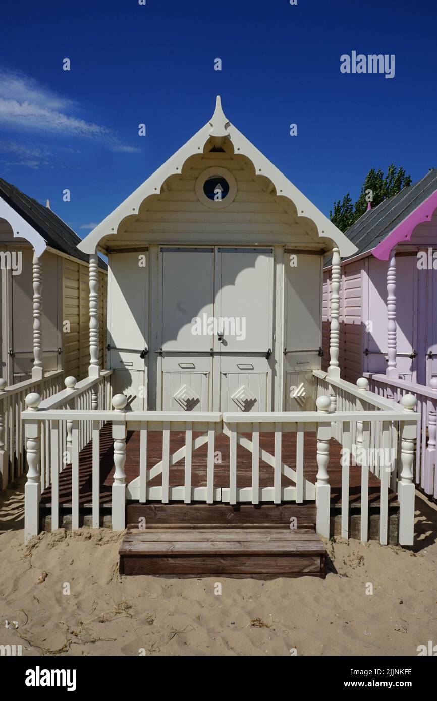 The picture shows a row of brightly coloured beach huts lining a sandy ...
