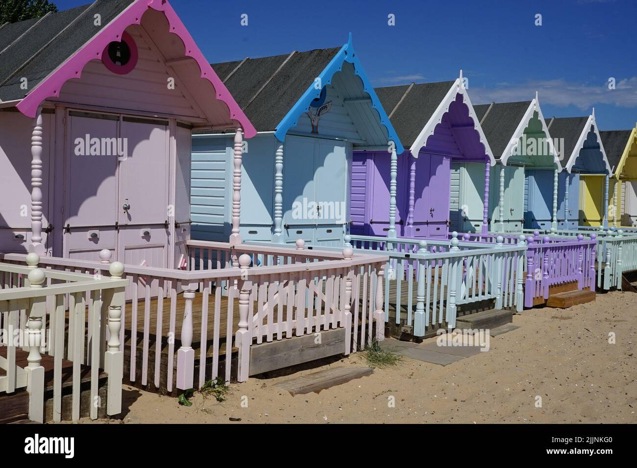 The picture shows a row of brightly coloured beach huts lining a sandy ...