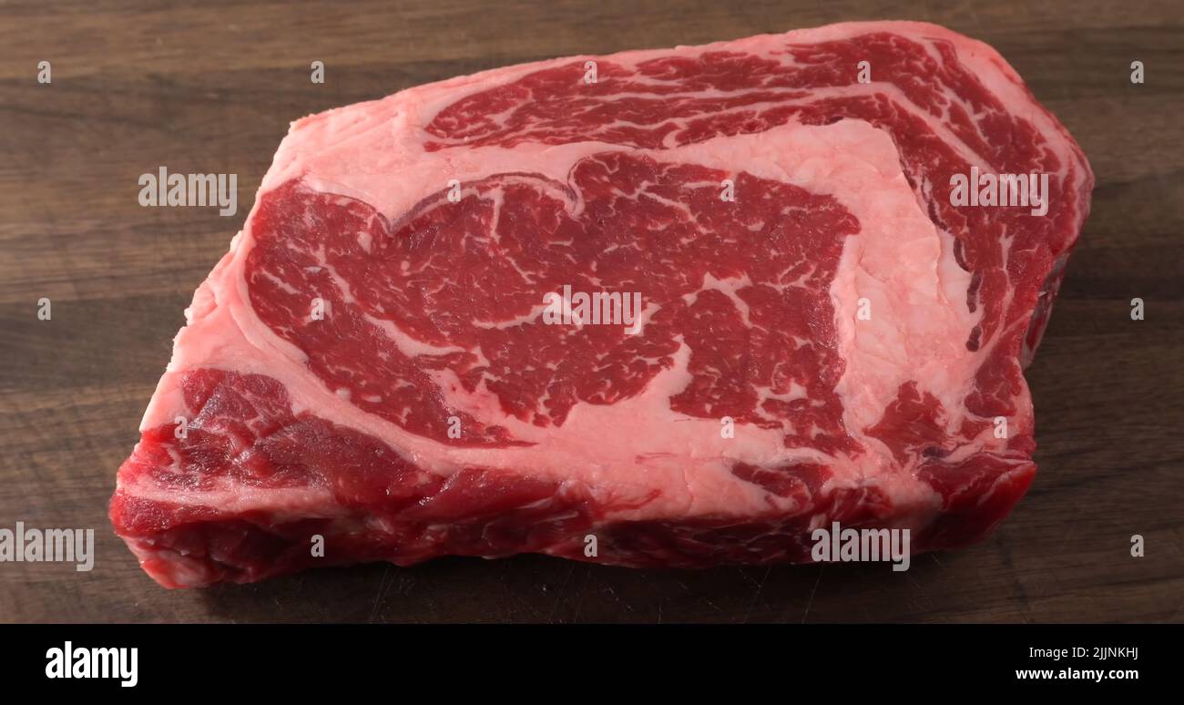 A closeup shot of a raw strip beef steak meat put on a wooden kitchen table Stock Photo