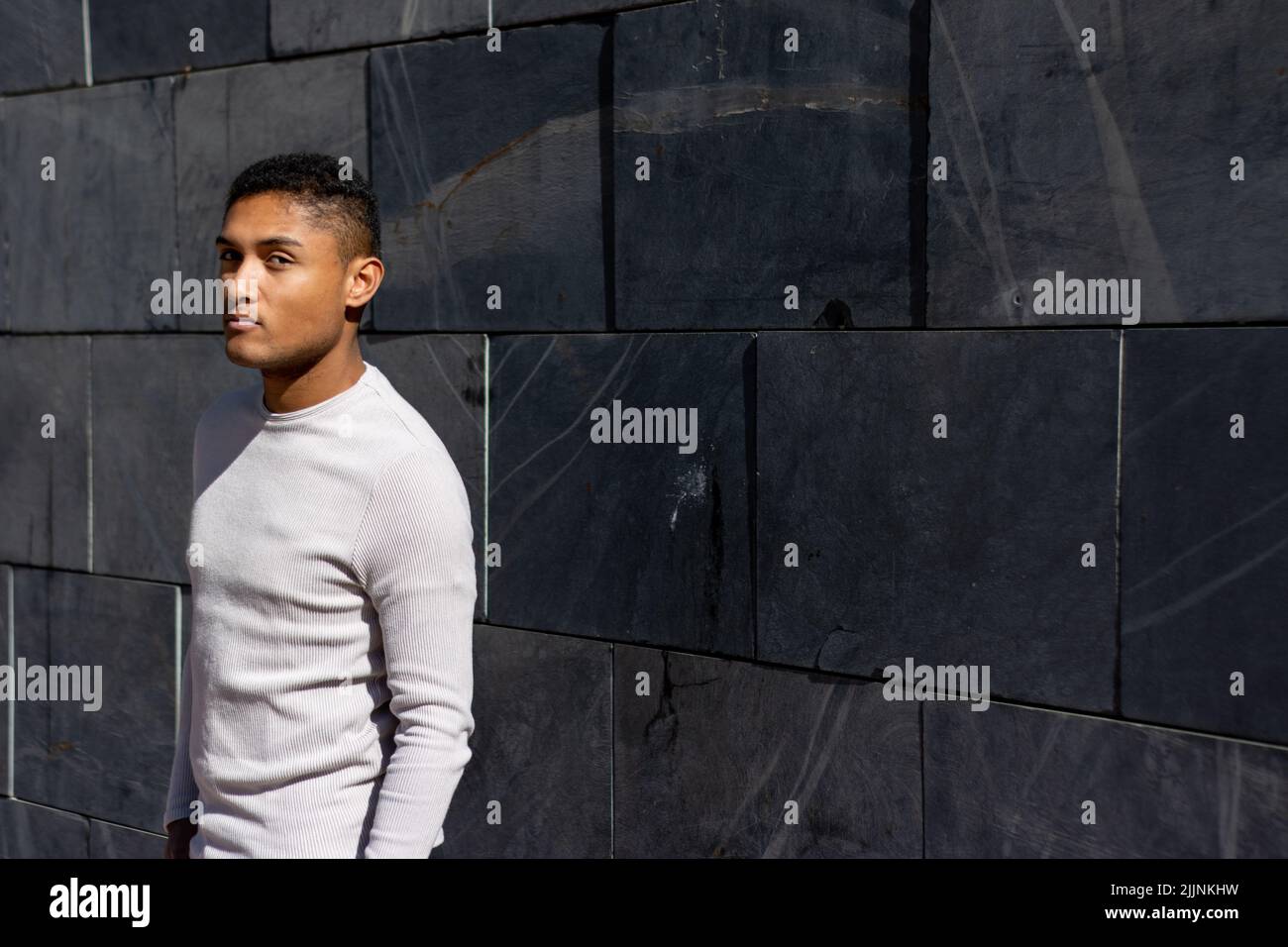 A Hispanic man posing white pullover, horizontal flagstone background with copy space Stock Photo