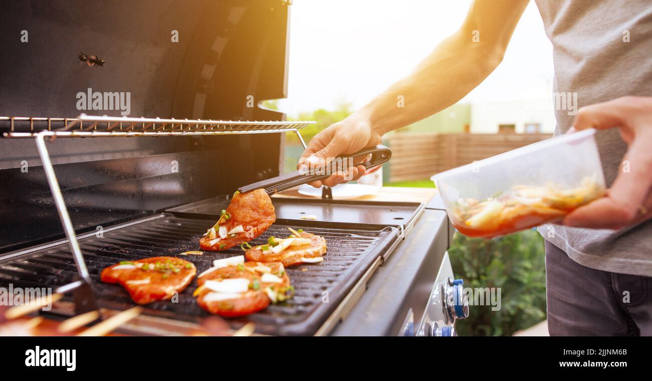 A young man hand is grilling some meat and vegetable skewers on a huge