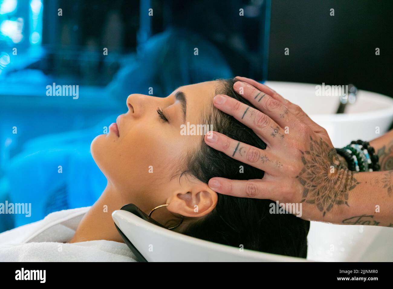 A closeup shot of a female relaxing while her hair is being washed at a salon by a tattooed stylist Stock Photo