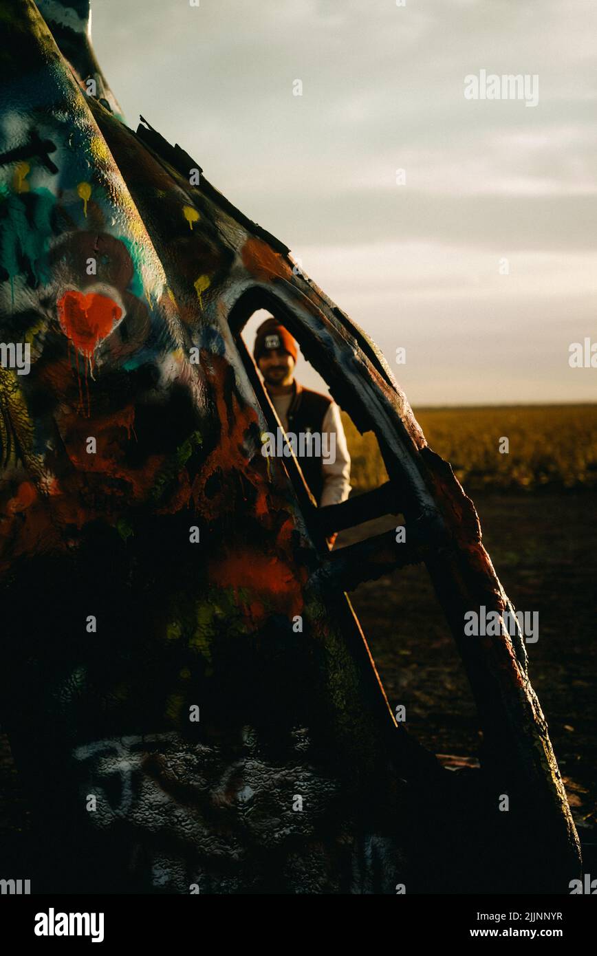 A vertical shot of a man seen through the window of a colorful car at Cadillac Ranch in Amarillo, Texas Stock Photo