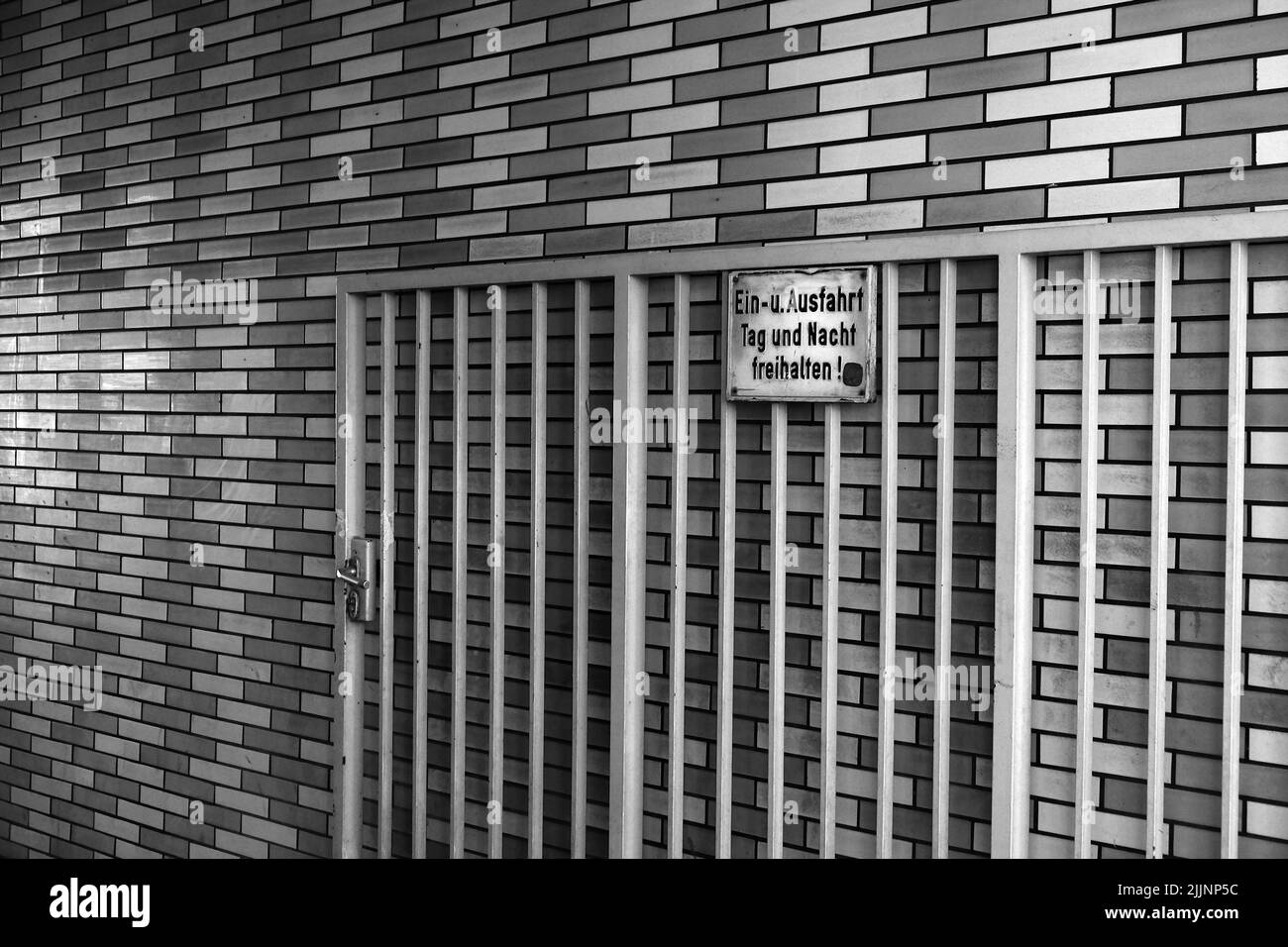 A grayscale of the metal gate opened and leaned on a brick wall Stock Photo
