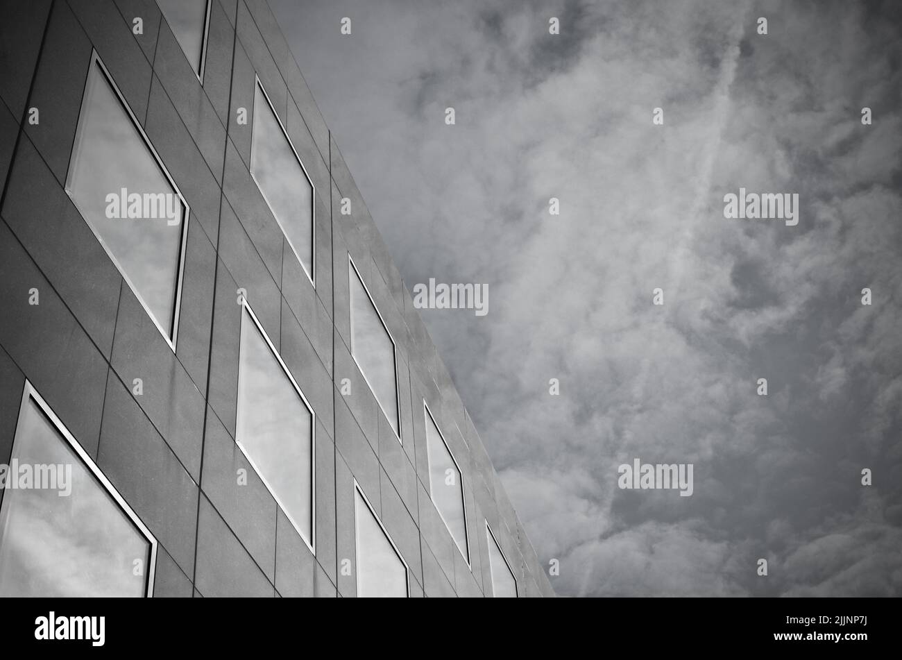 A low angle shot of a modern building under a cloudy sky in grayscale ...