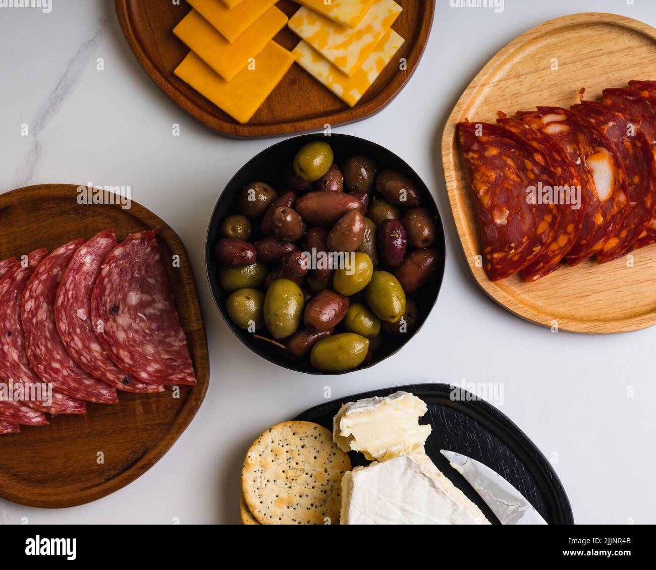 An overhead shot of various meats and cheeses with crackers on white marble surface Stock Photo