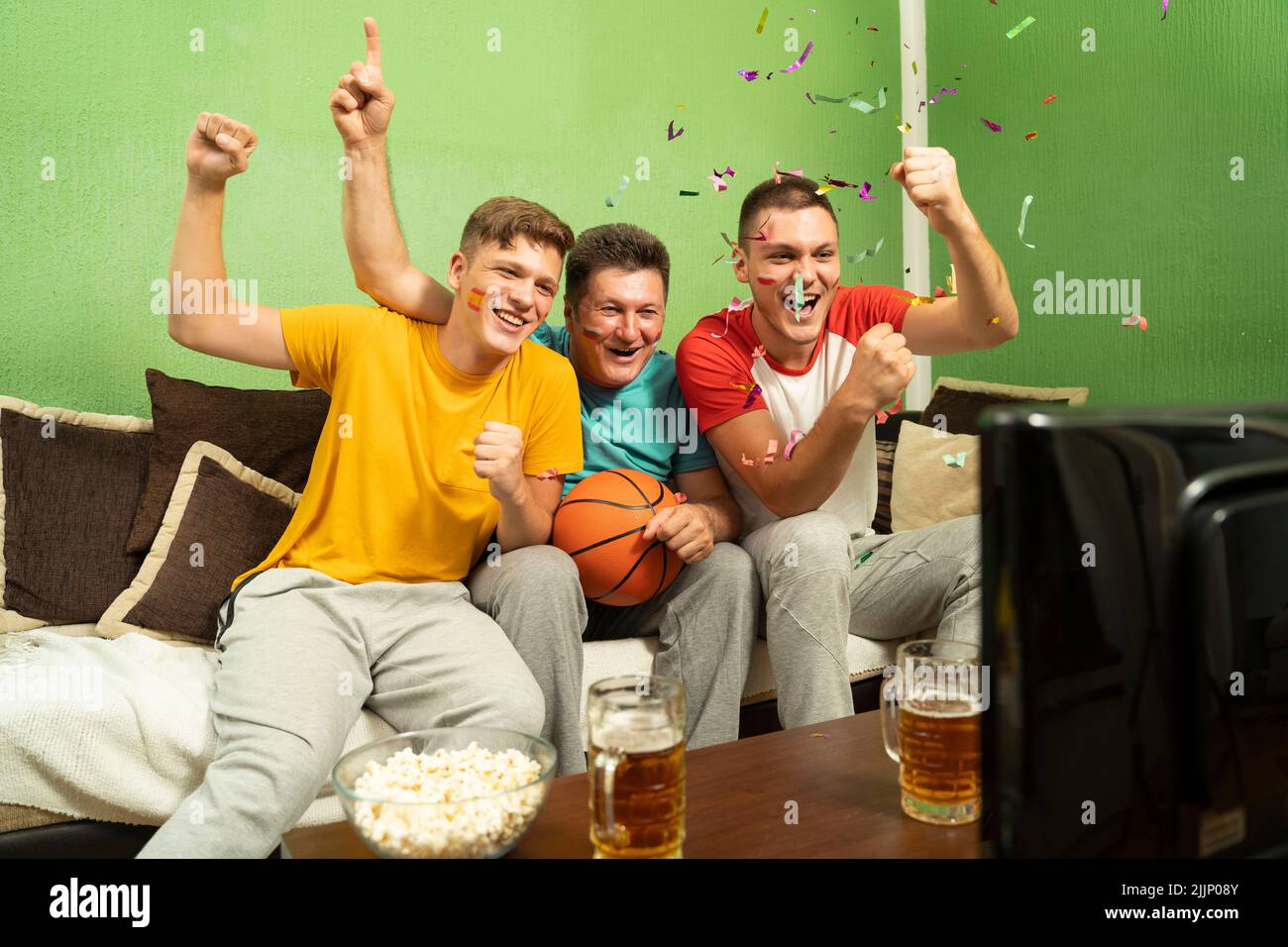 Three male basketball fans watching the game and celebrating victory Stock Photo